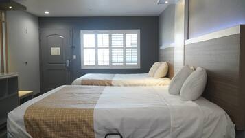 Een hotelkamer met twee bedden, een raam met zonwering, een deur met slot en een nachtkastje.