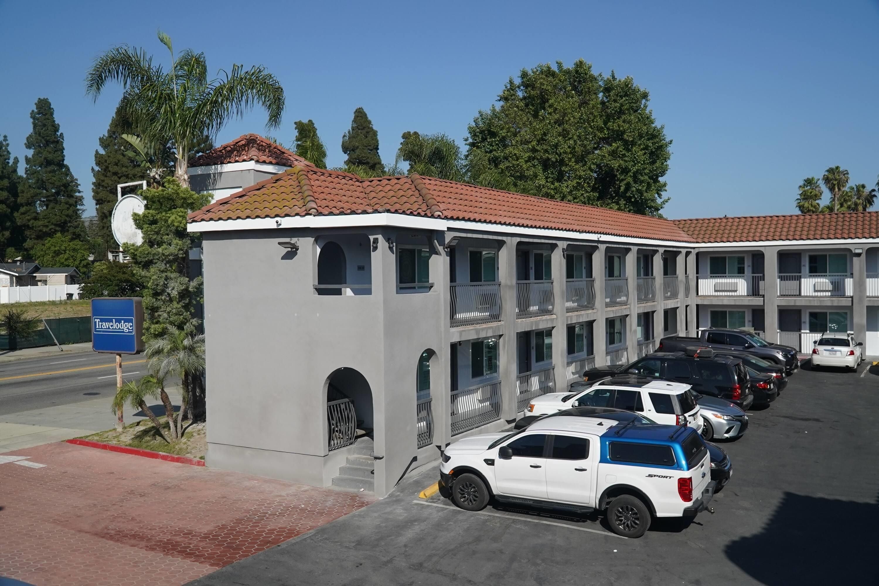 A Travelodge hotel with a parking lot, multiple cars, and surrounding greenery.
