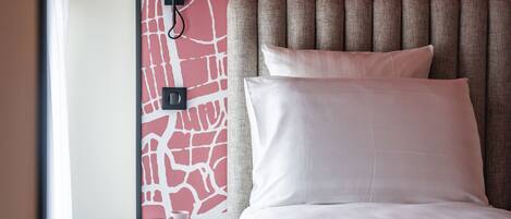 A hotel room with a bed, a bedside table with a lamp, and a wall with a red abstract design.