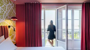 A hotel room with a bed, red curtains, a large window, and a view of the outside. - Le Grand Hotel By Stay Collection (Strasbourg)