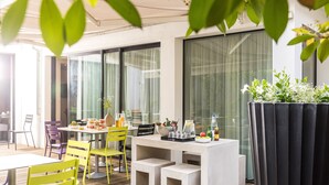 An outdoor dining area with a table set for two, surrounded by yellow chairs, and a planter with flowers to the right. - Le Grand Hotel By Stay Collection (Strasbourg)