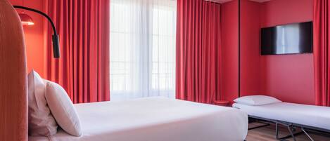 A modern hotel room with a large bed, a smaller bed, a TV, and red curtains.