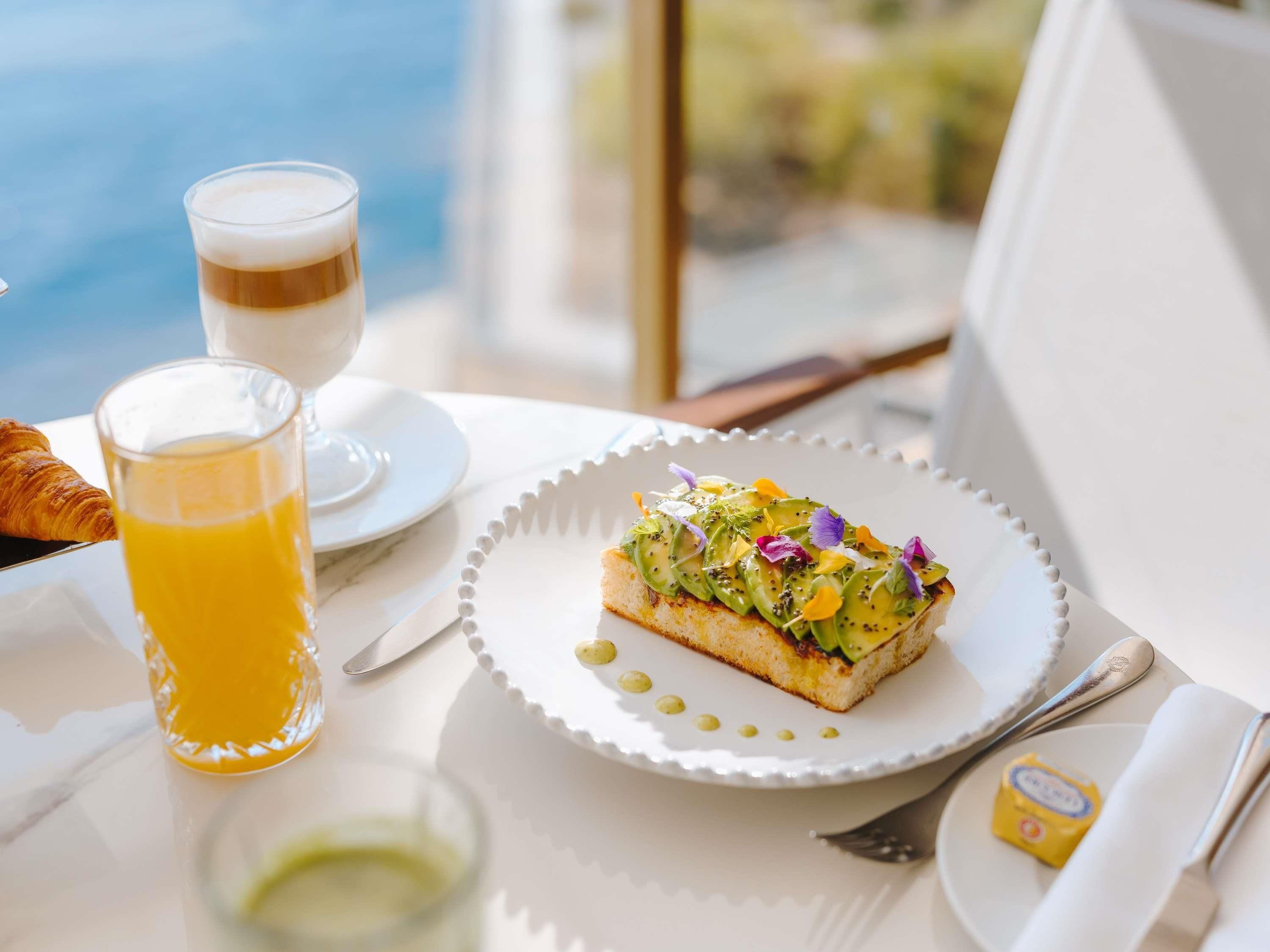 A breakfast setting with a croissant, a glass of orange juice, a glass of coffee, and a plate with a decorated pastry.