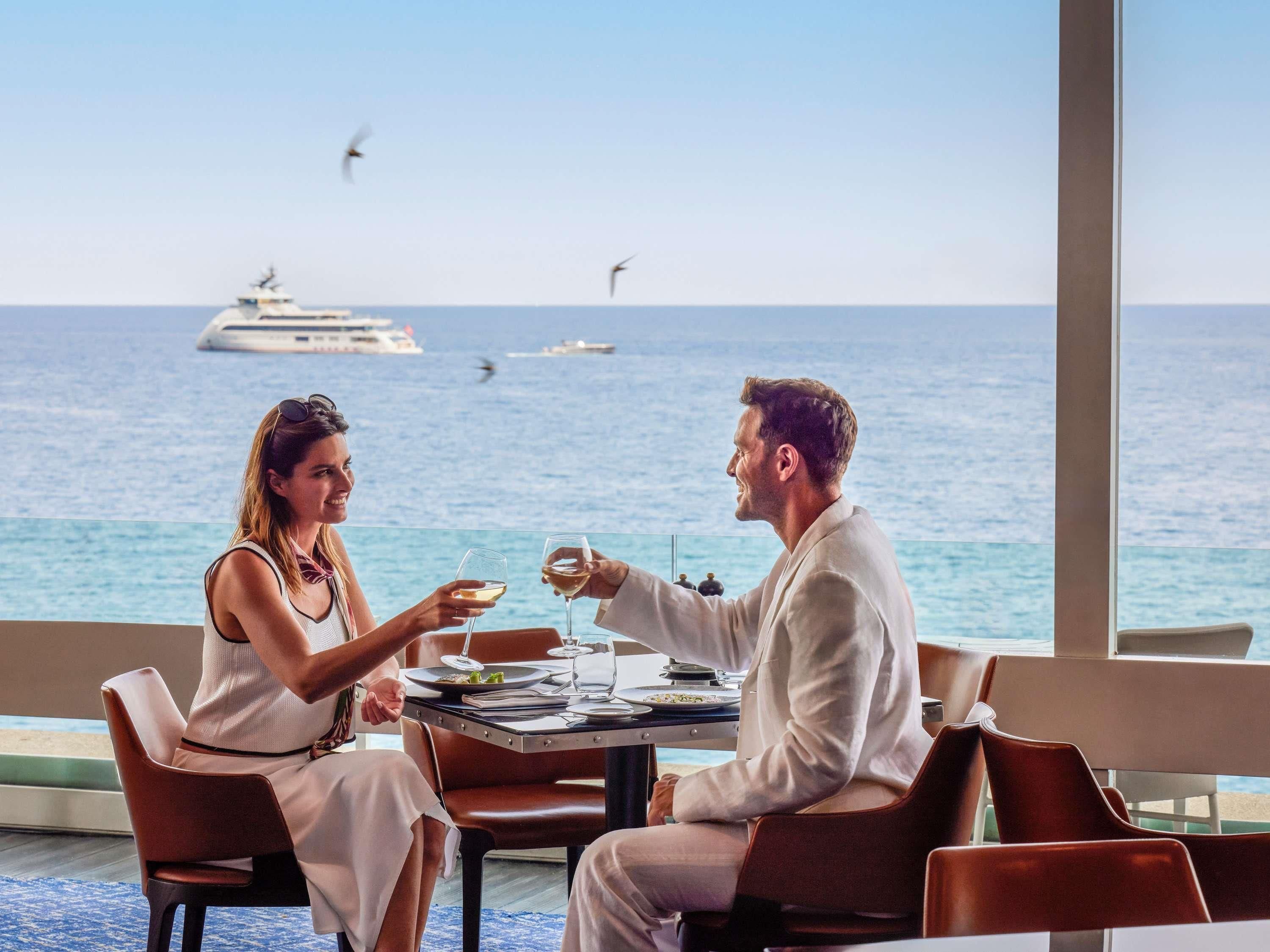 A couple dining at a table with a view of the sea and boats.