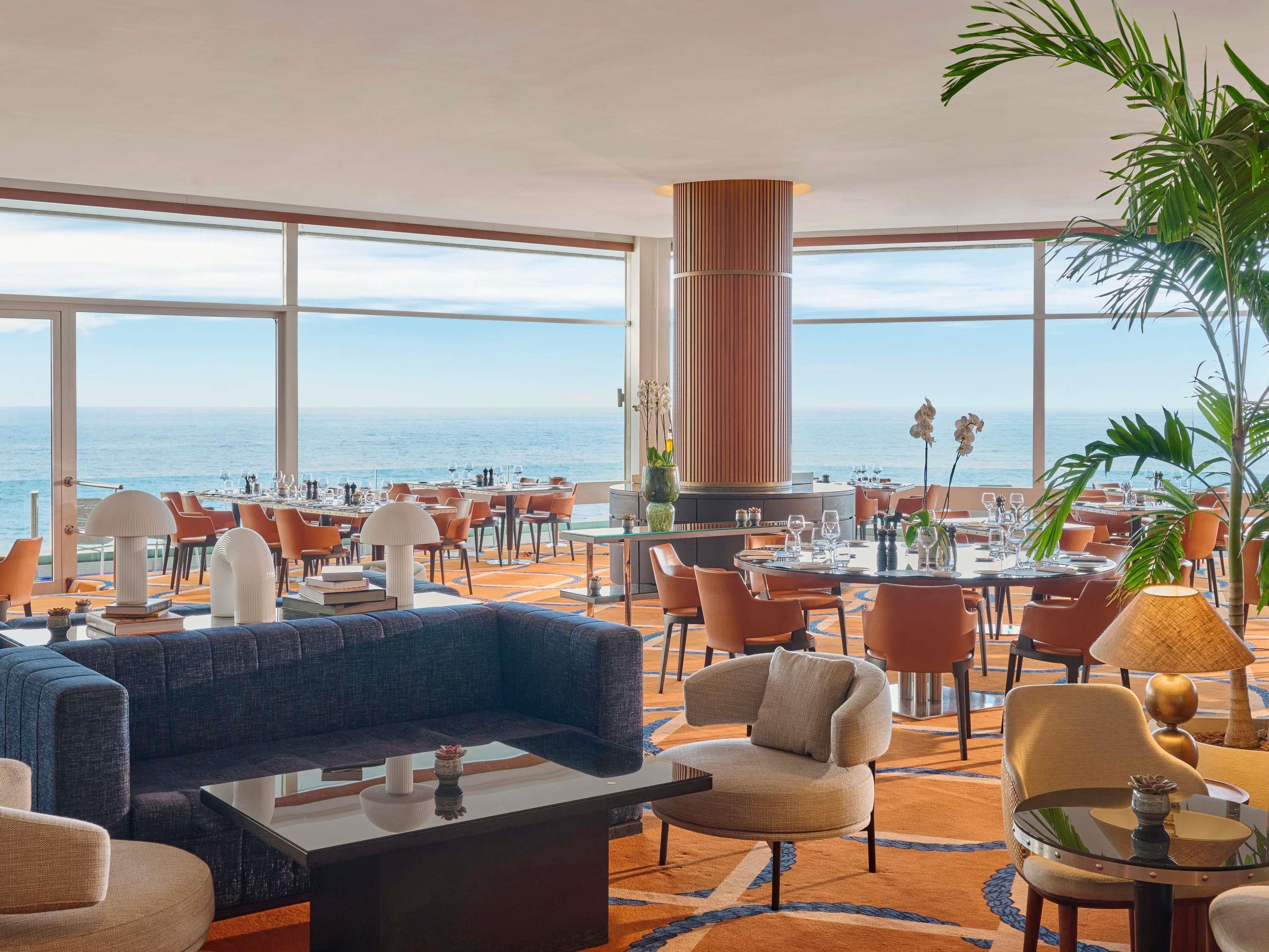 Un hall d’hôtel doté d’un grand espace salon, d’un bar et offrant une vue sur la mer.