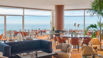 Un hall d’hôtel doté d’un grand espace salon, d’un bar et offrant une vue sur la mer.