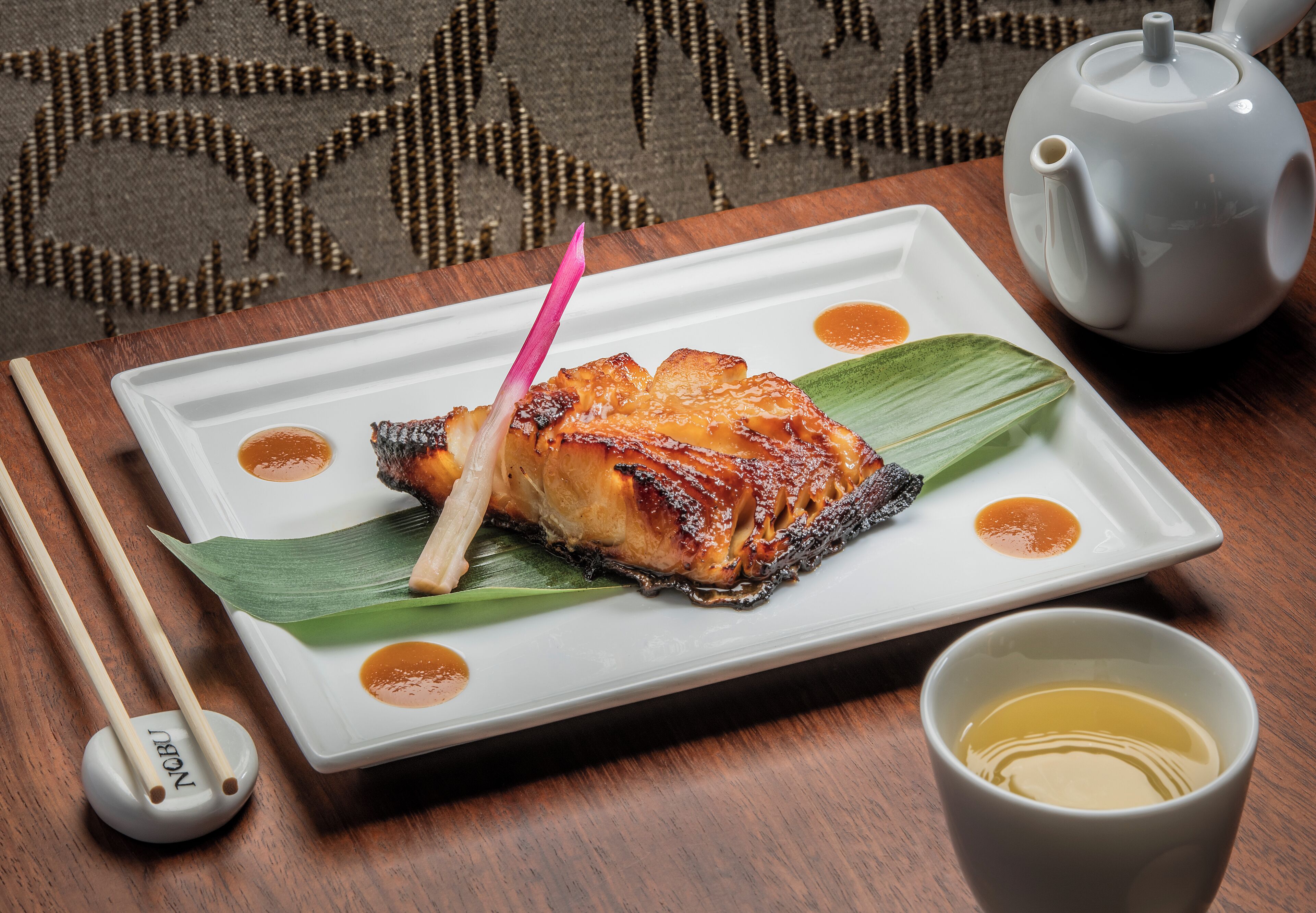A plate of food with chopsticks and a teapot on a table.