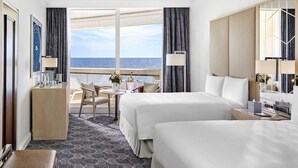 Camera d'albergo con due letti, una scrivania, una sedia, un tavolino con un vaso e vista sul mare.