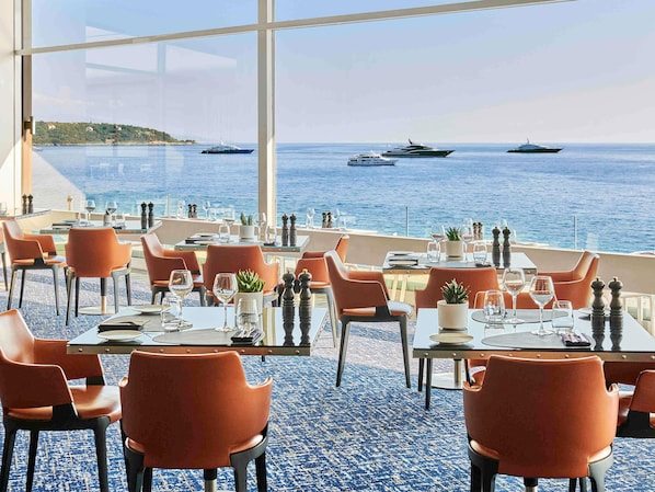 A restaurant with tables and chairs, a view of the sea, and boats in the distance. - Fairmont Monte Carlo (Monaco)