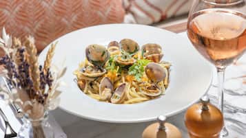 A plate of pasta with clams garnished with parsley, a glass of rosé wine, and a salt and pepper shaker on a table.
