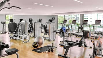 Un gimnasio con diverso equipo de ejercicio, un ventanal grande y piso de madera.