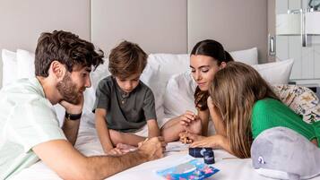 Una familia de cuatro personas en una habitación de hotel con una cama, almohadas, una mesita de noche y una almohada decorativa con diseño de ballena.