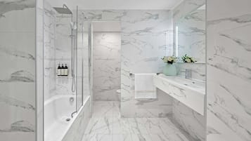 A modern bathroom with a glass-enclosed shower, a marble-tiled floor, and a vanity with a mirror and a vase of flowers.