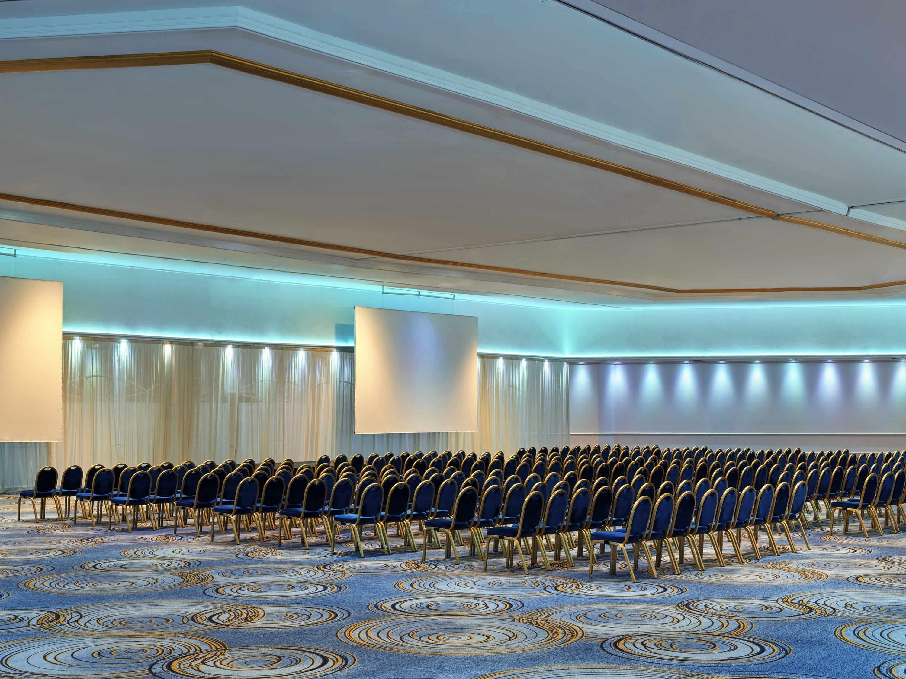 Un salón de conferencias con filas de sillas azules y una alfombra estampada.