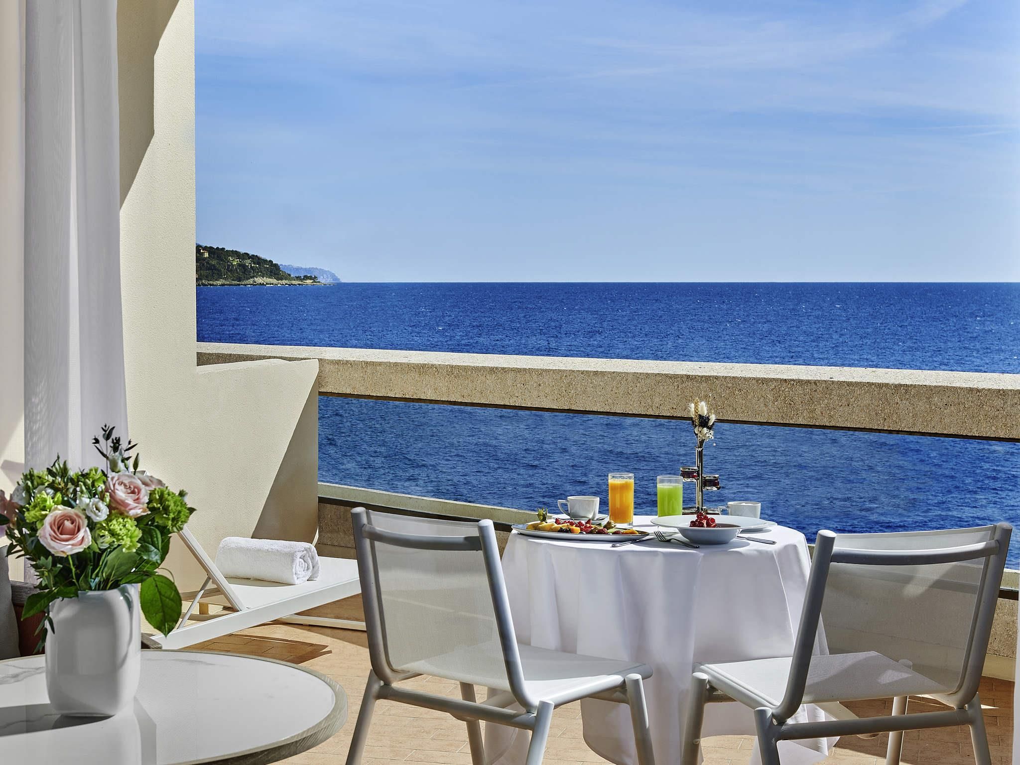 A table set with breakfast on a balcony overlooking the sea.