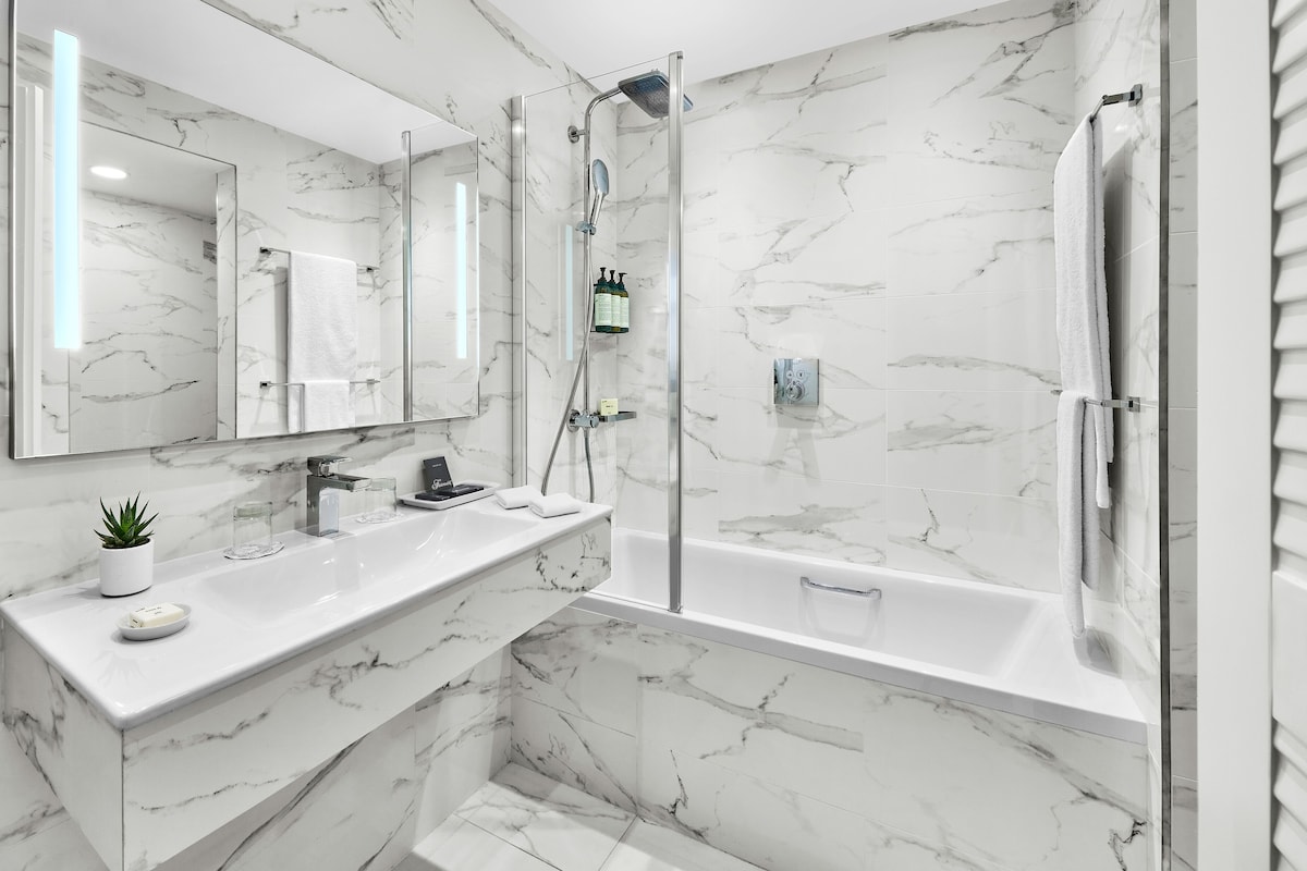 A modern bathroom with a marble countertop, a glass shower enclosure, and a bathtub.