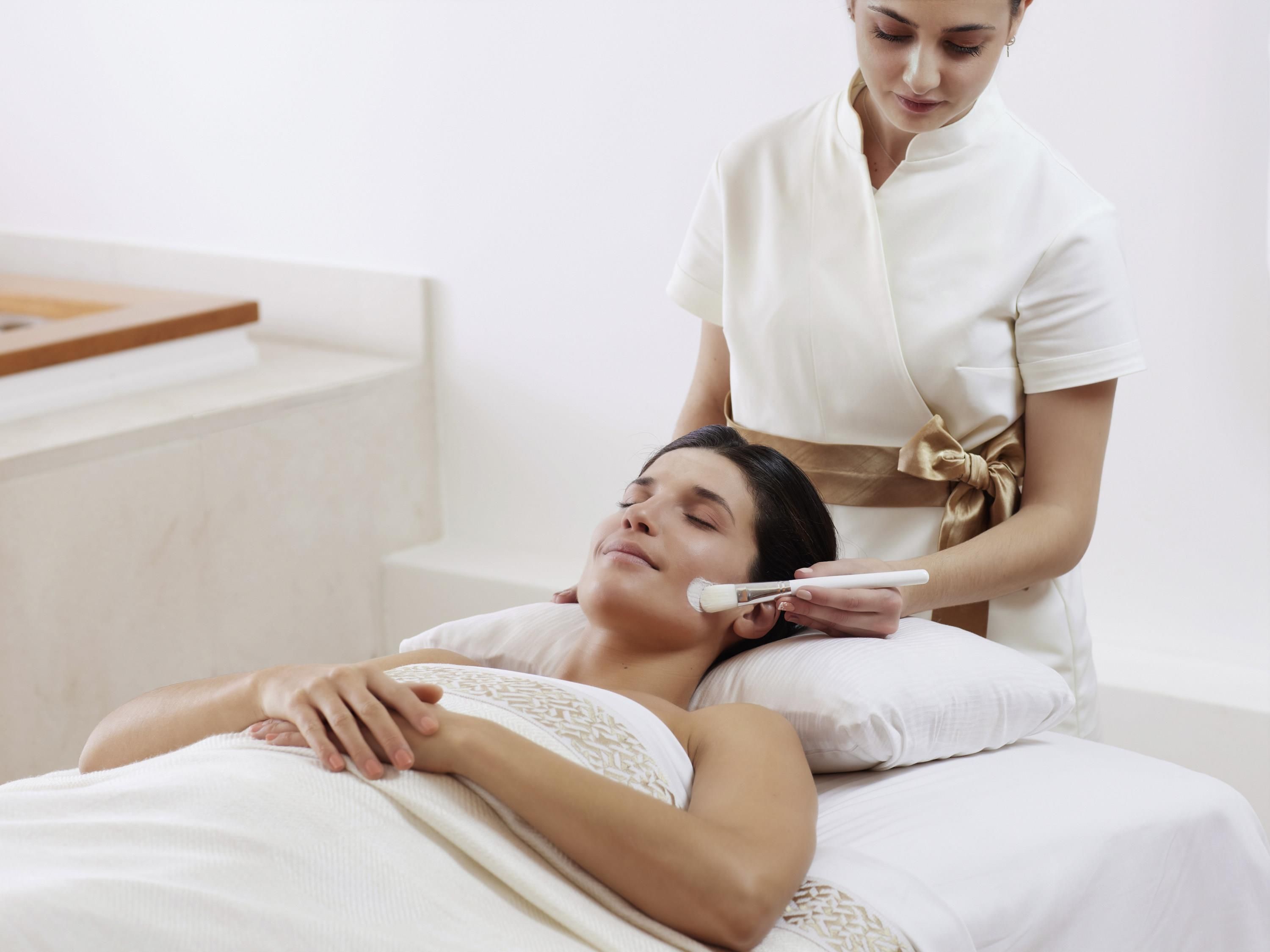 A person lying on a bed in a room with a white bedspread and a wooden headboard.