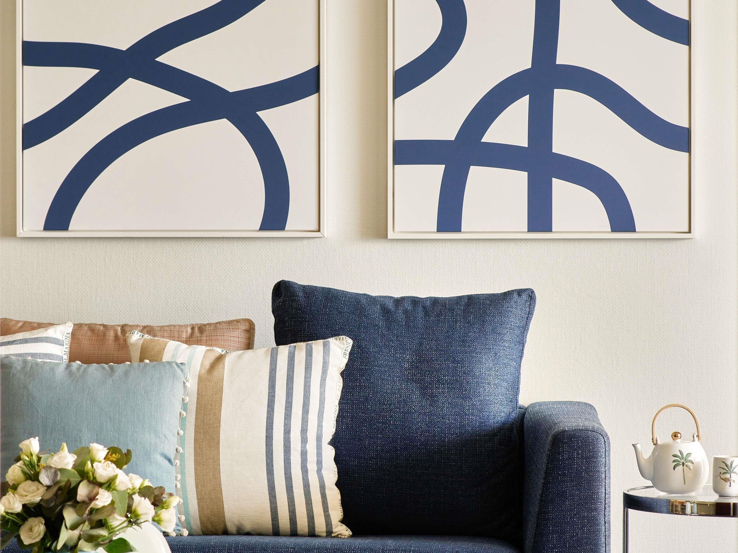 A room with a sofa, decorative pillows, a vase of flowers, and two abstract paintings on the wall.