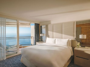Une chambre d’hôtel avec un grand lit, une table de chevet, un miroir et une vue sur la mer.