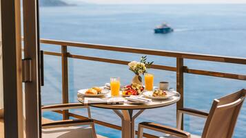 Una mesa en el balcón con desayuno, un jarrón de flores y vista al mar.