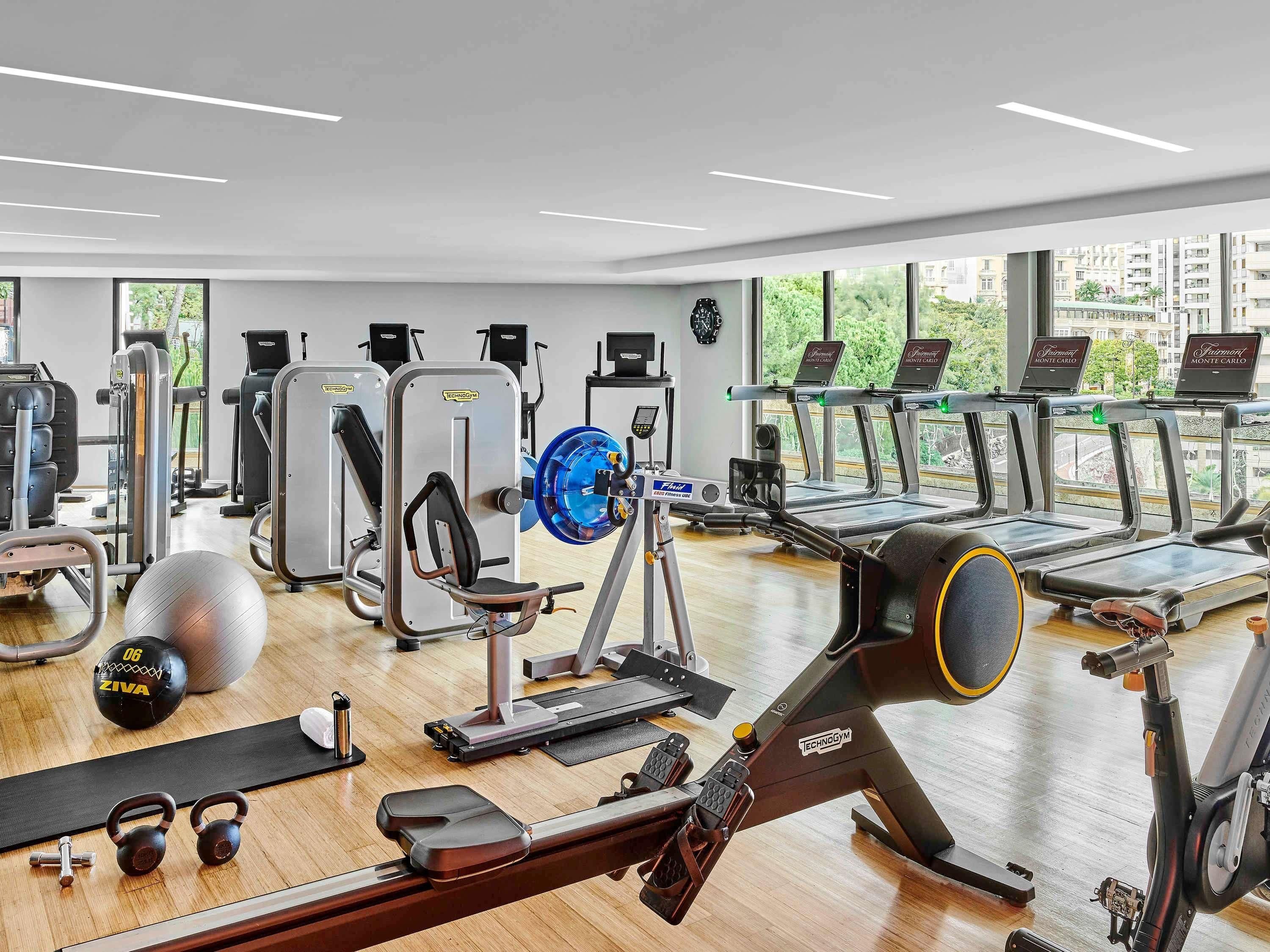 A gym with cardio machines, weightlifting equipment, and a large window providing a view of the city.