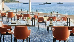Un ristorante con tavoli e sedie, vista sul mare e barche in lontananza.