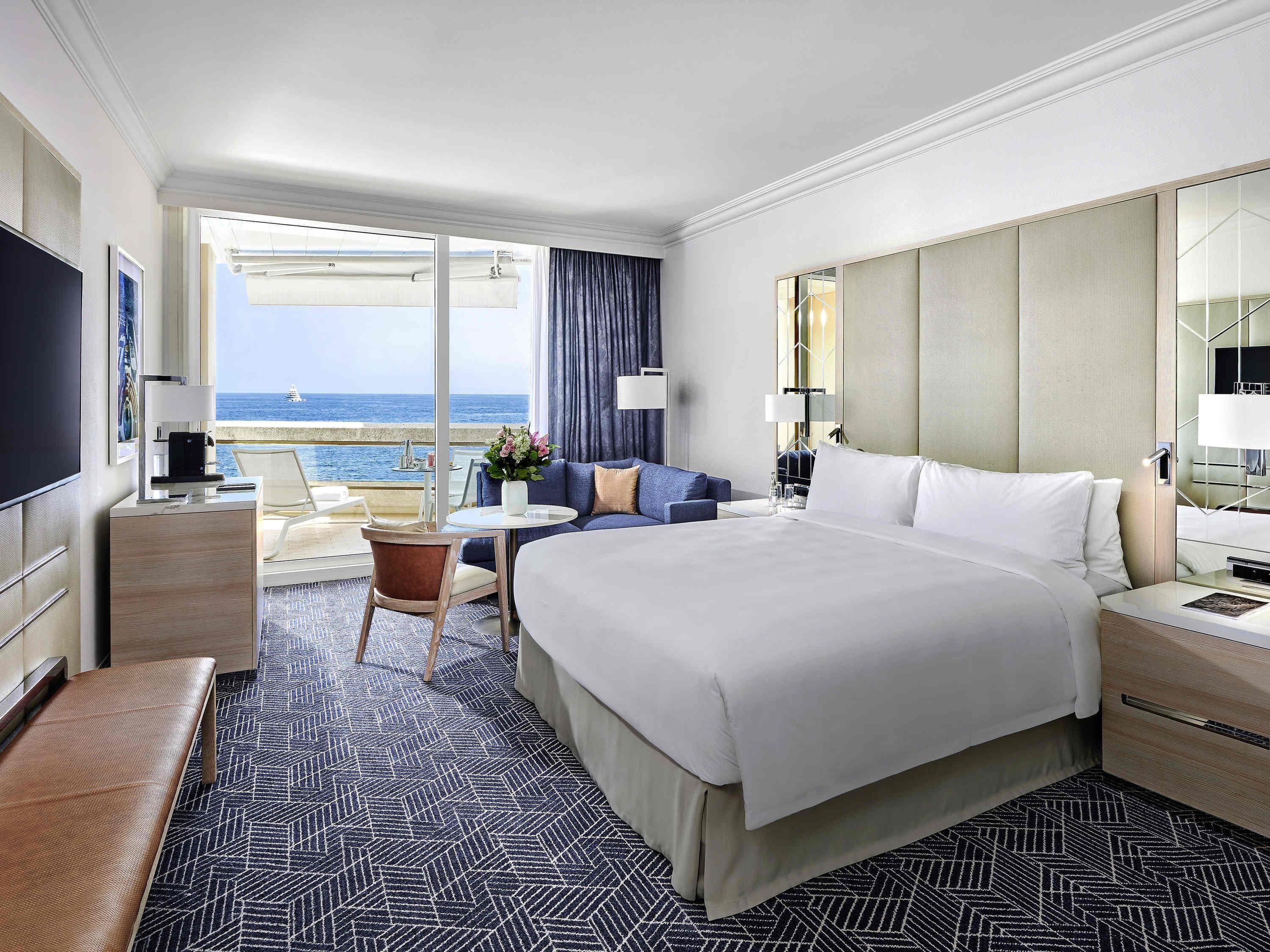 Une chambre d’hôtel avec un grand lit, un bureau, une chaise et un balcon donnant sur la mer.