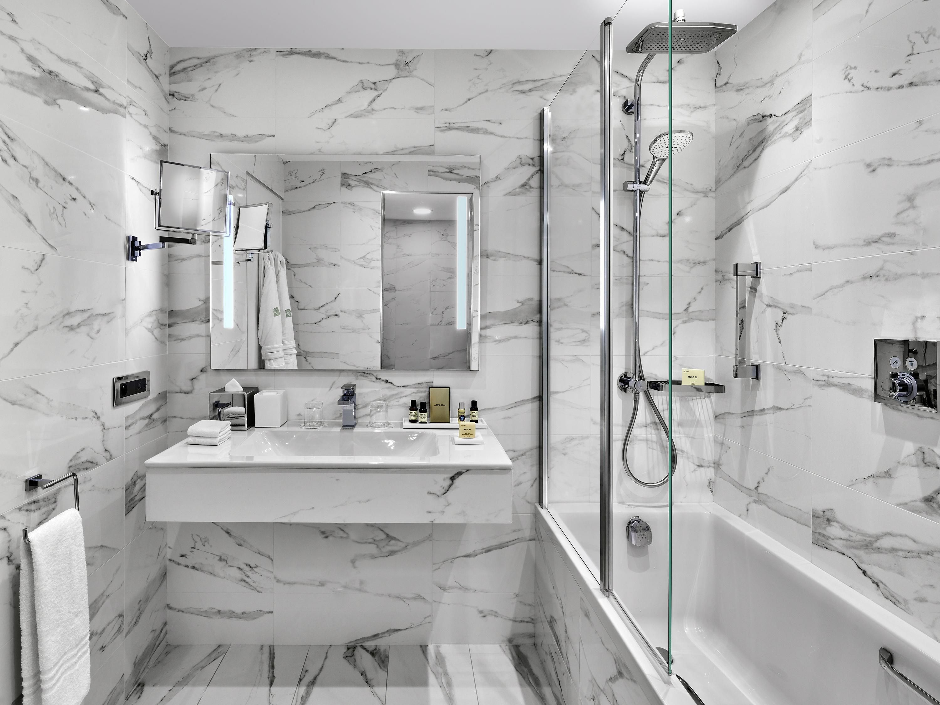 Een moderne badkamer met marmeren wanden, een douche met glazen wanden en een wastafel met spiegel en handdoekrek.