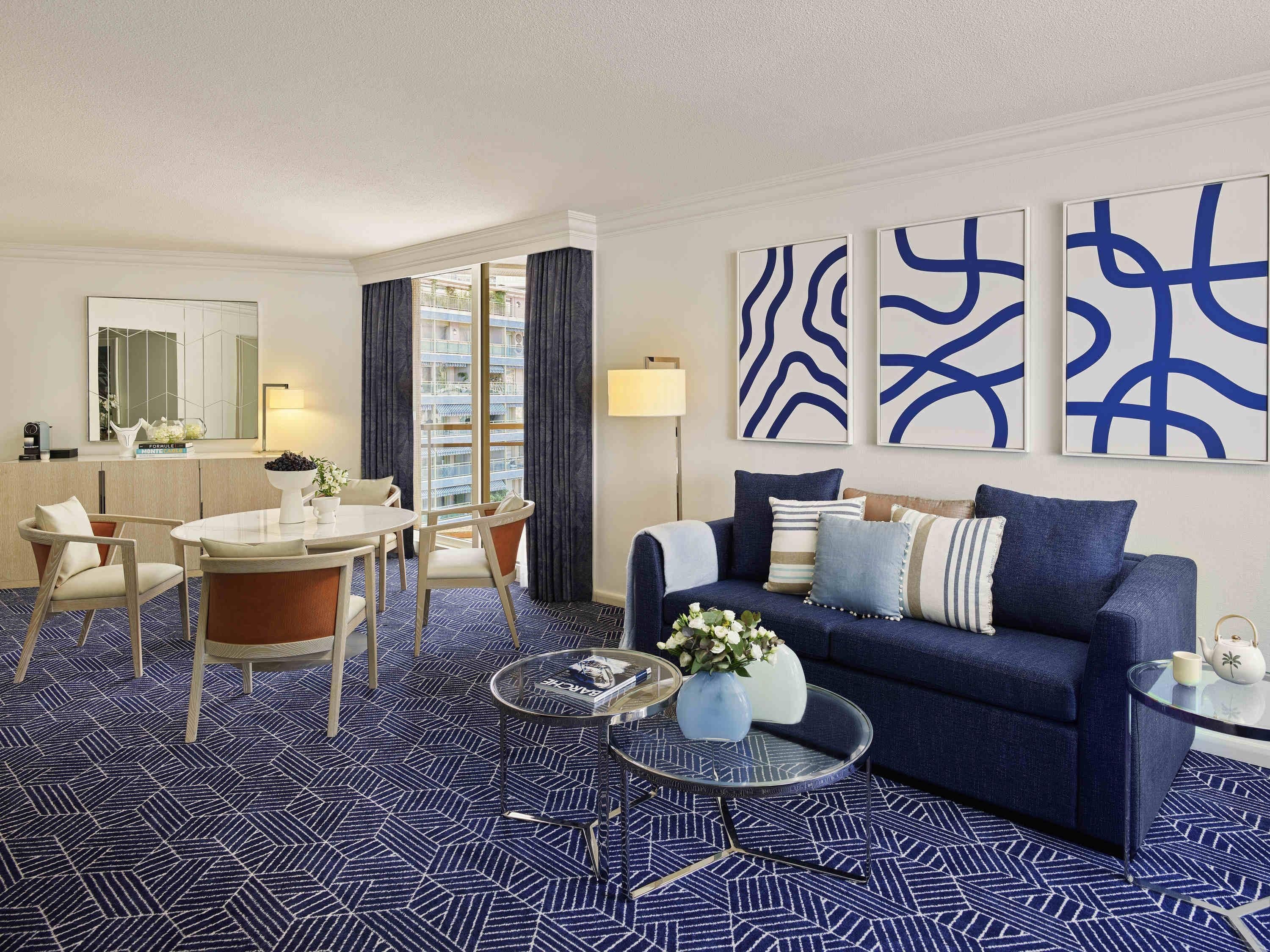 A modern hotel room with a dining area, a sofa set, and abstract wall art.