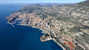 Vista aérea de una ciudad costera con una zona urbana densa, un puerto deportivo y terreno montañoso circundante.