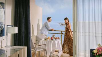 Una habitación con balcón que da al mar, una mesa de comedor con comida y vista a yates.