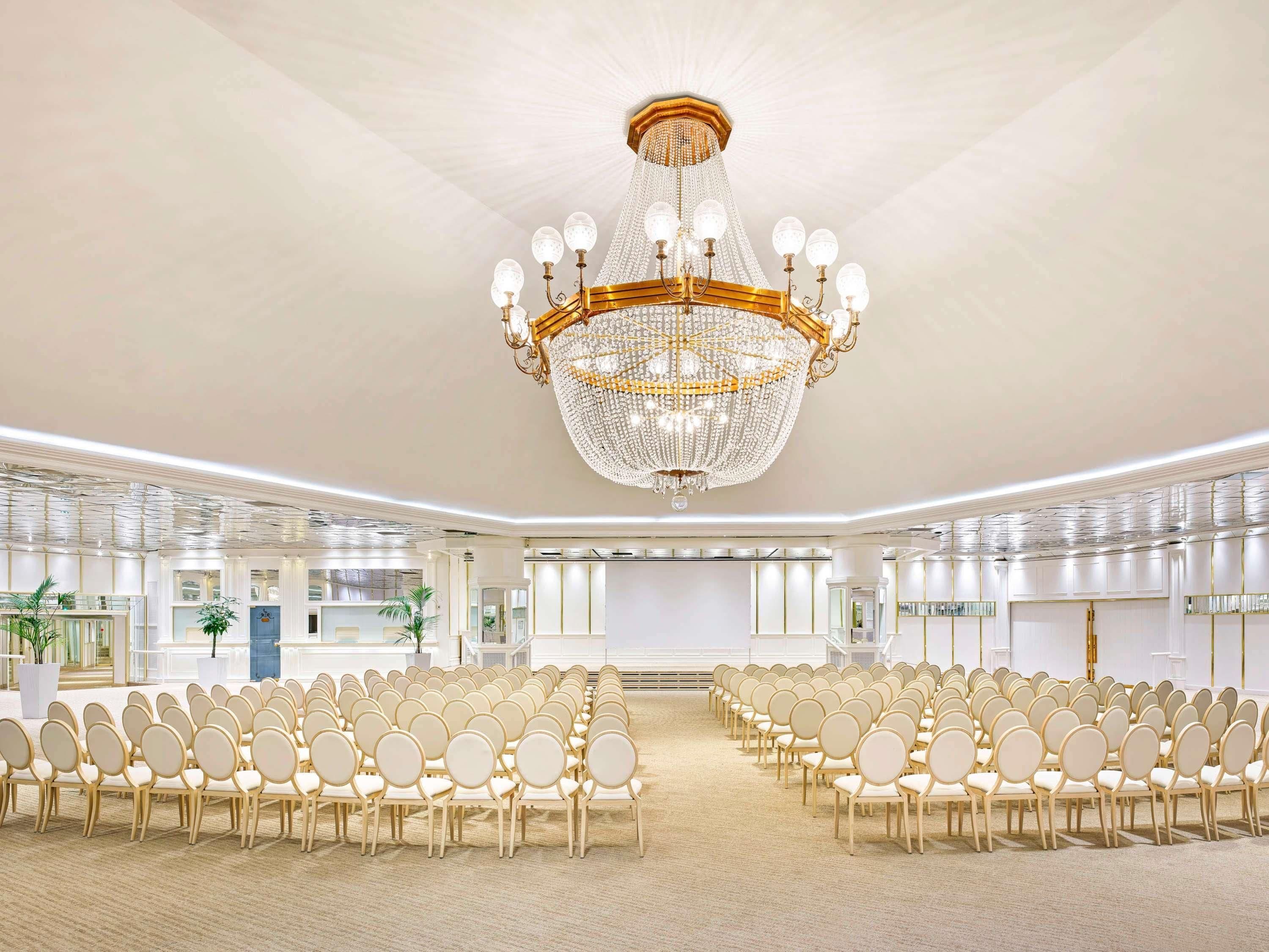 A large conference room with rows of chairs, a grand chandelier, and a modern ceiling design.