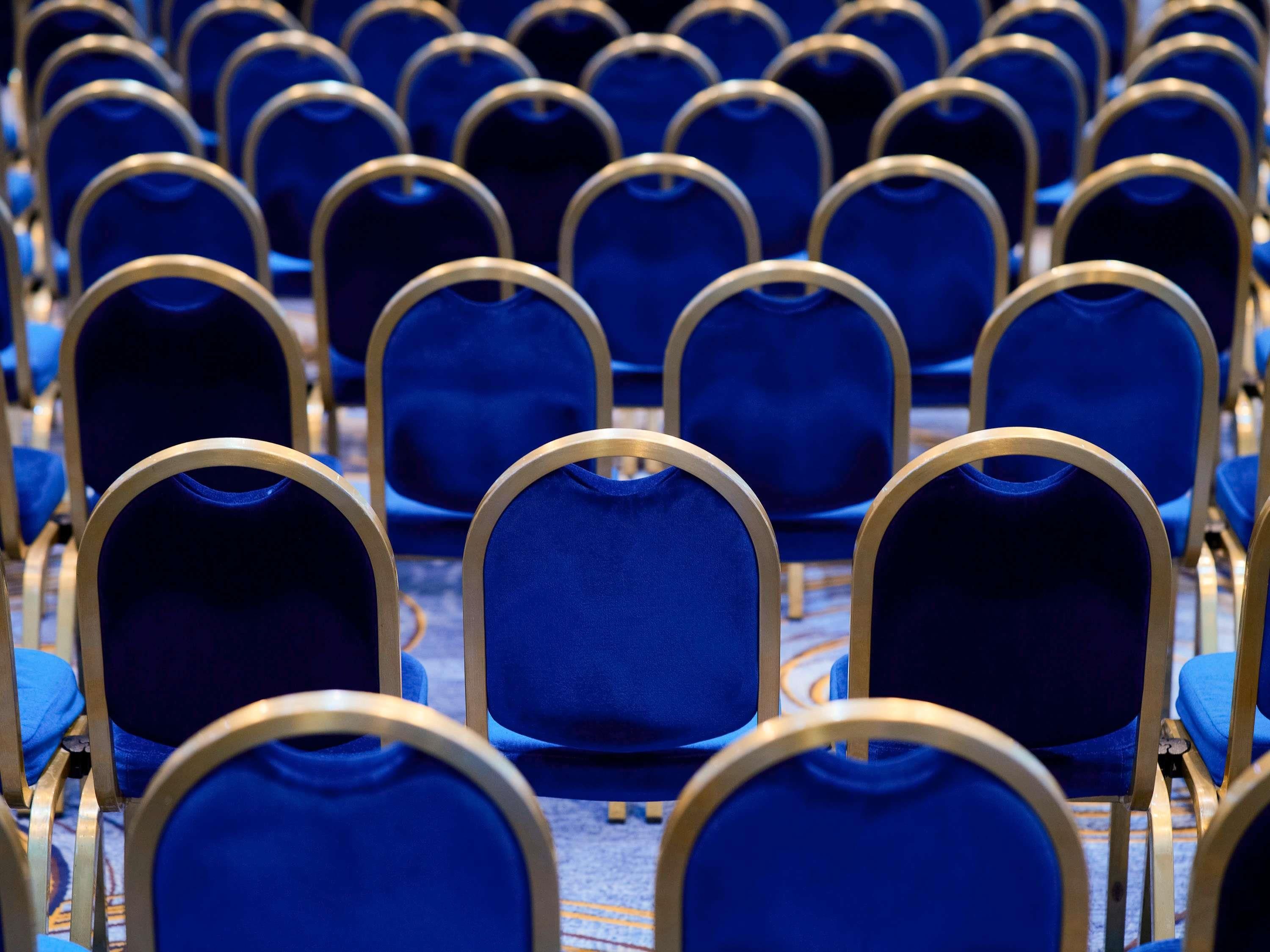 Rows of blue chairs with gold frames in a conference room.