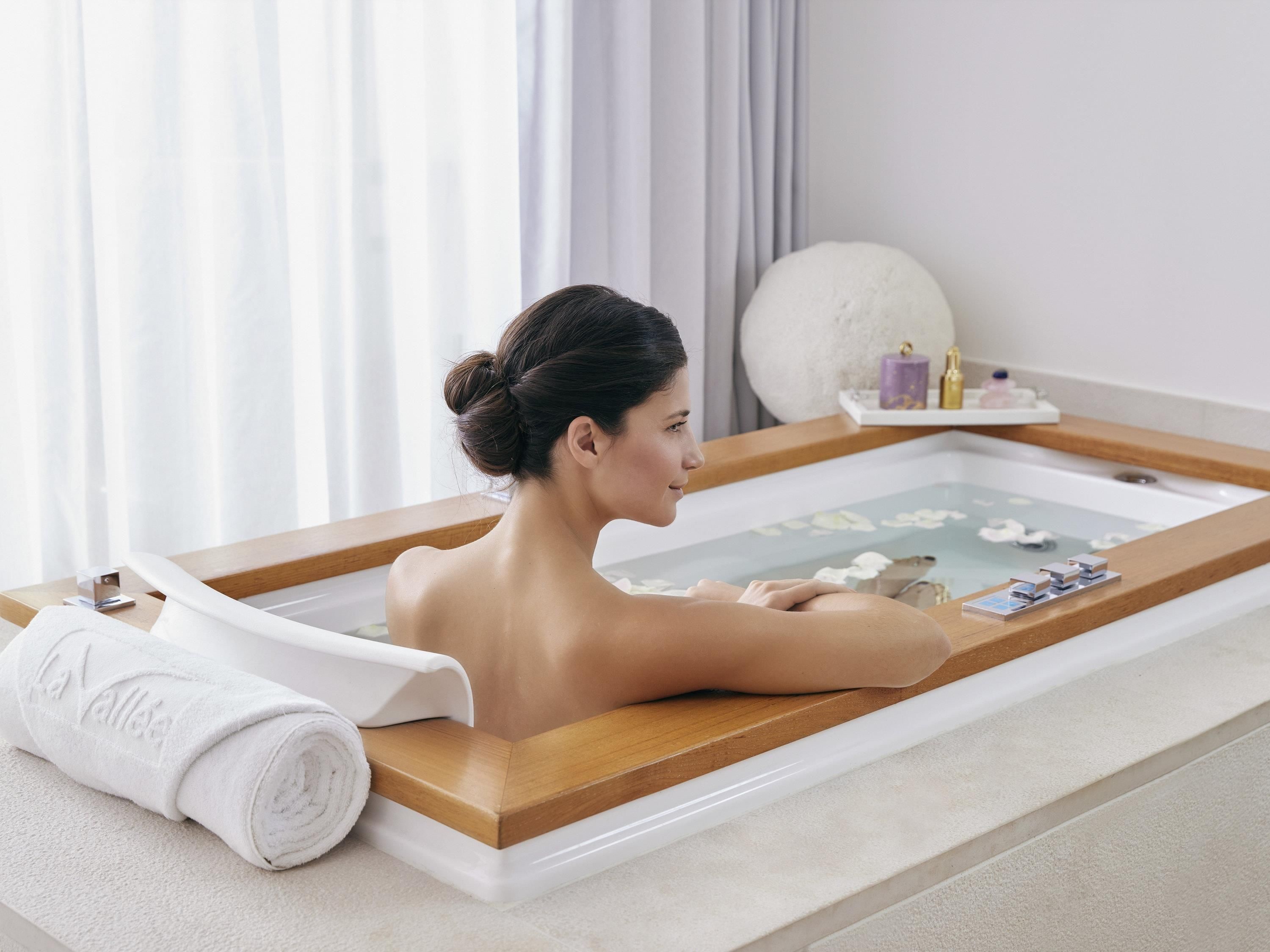 A person relaxing in a bathtub with a towel and bath products on the side.