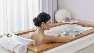 A person relaxing in a bathtub with a towel and bath products on the side.