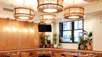 Un restaurante con mesas redondas y cabinas, paredes de madera y lámparas de mimbre colgantes.