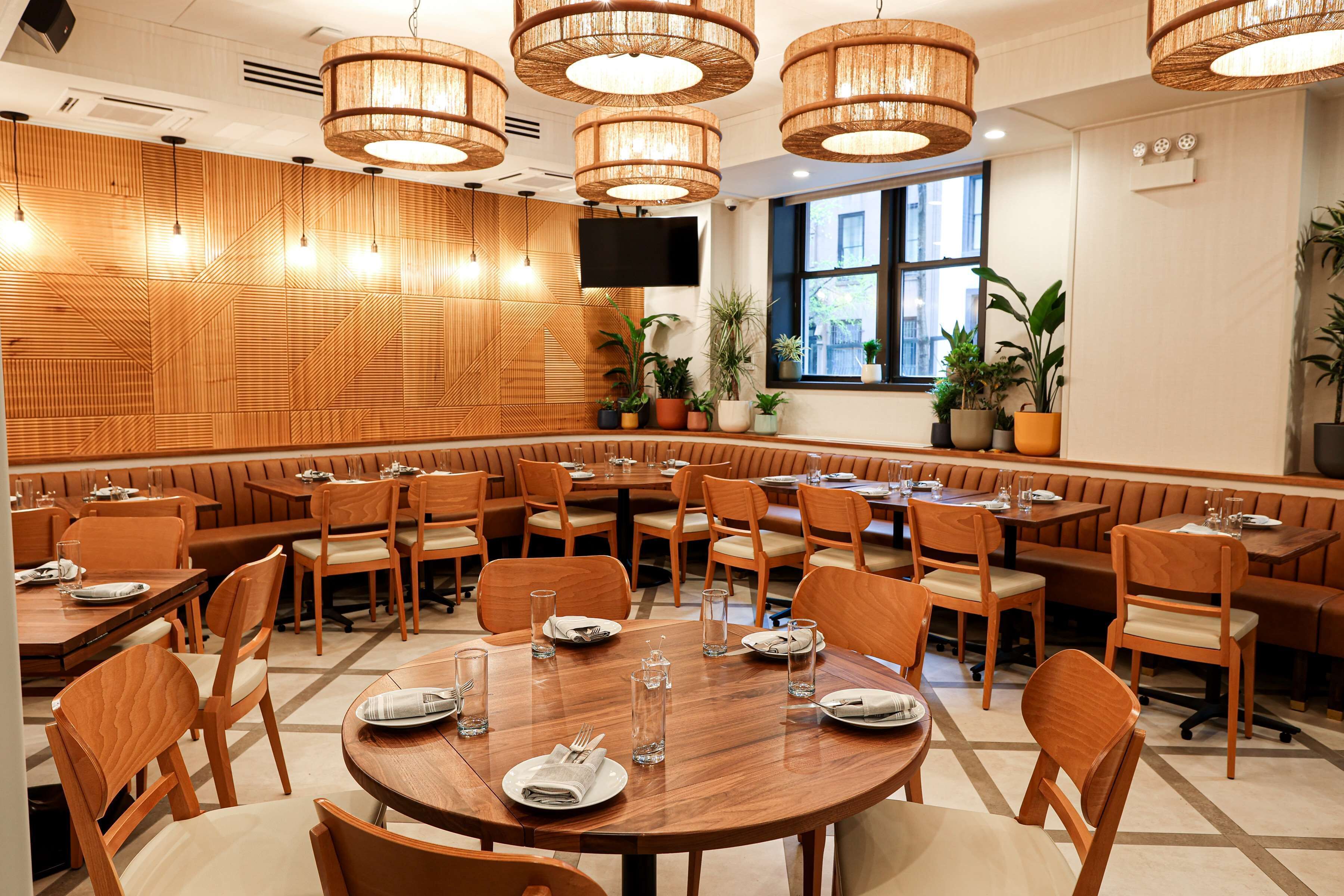 A restaurant with round tables, wooden walls, and hanging wicker chandeliers.