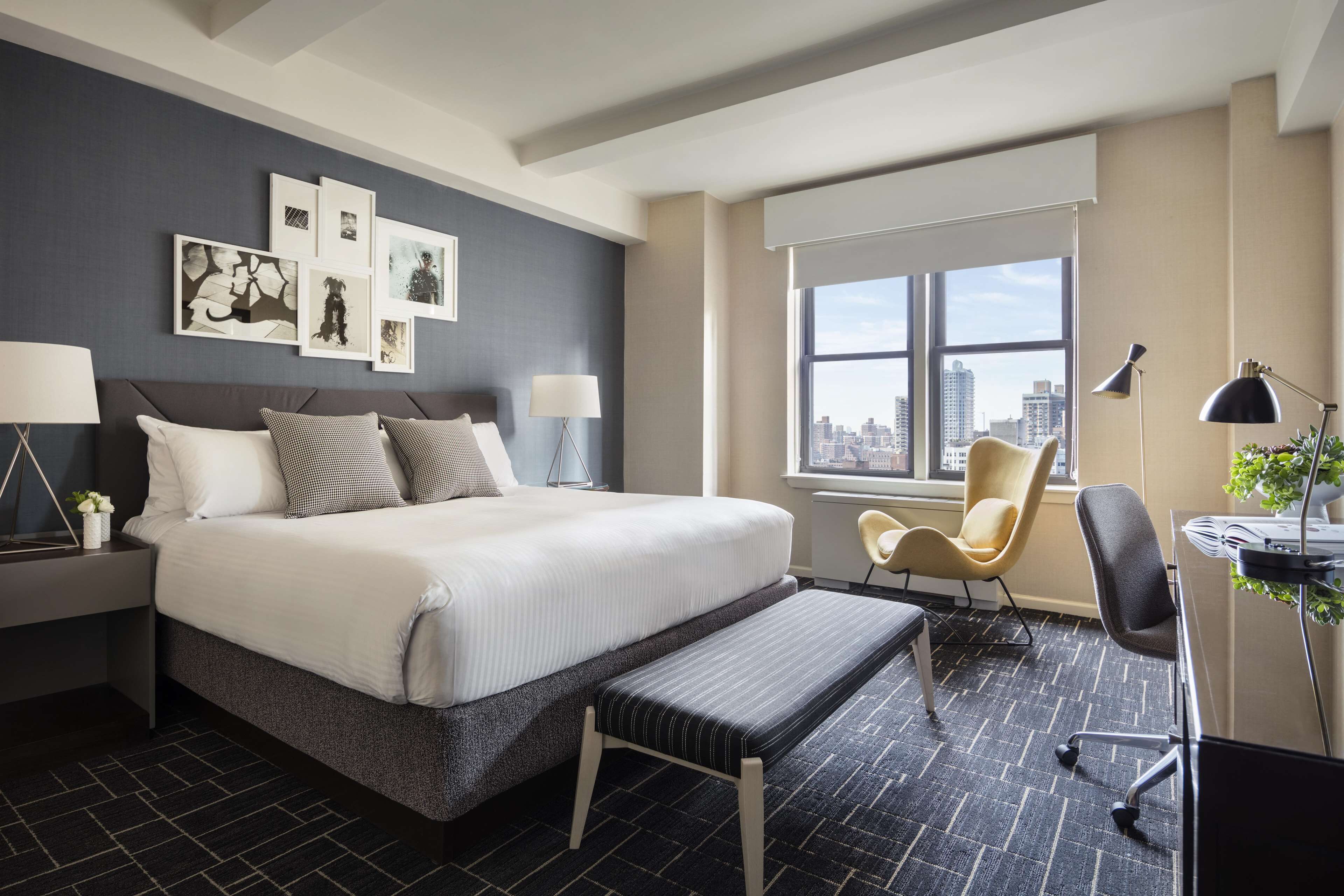 A modern hotel room with a large bed, a desk, a chair, and a window with a city view.