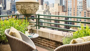 Une terrasse sur le toit, aménagée avec des meubles en osier, un grand vase décoratif et offrant une vue sur l’Empire State Building.
