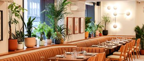 A restaurant with booths and tables, potted plants, and framed artwork on the walls.