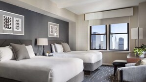 A hotel room with two beds, a desk, a chair, and a large window with a city view.