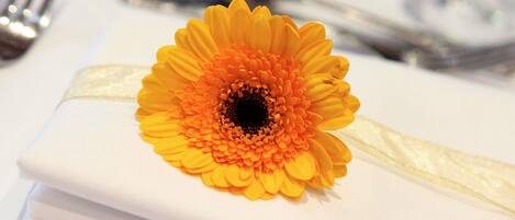 A table setting with a white tablecloth, a folded napkin, and a yellow flower boutonniere.