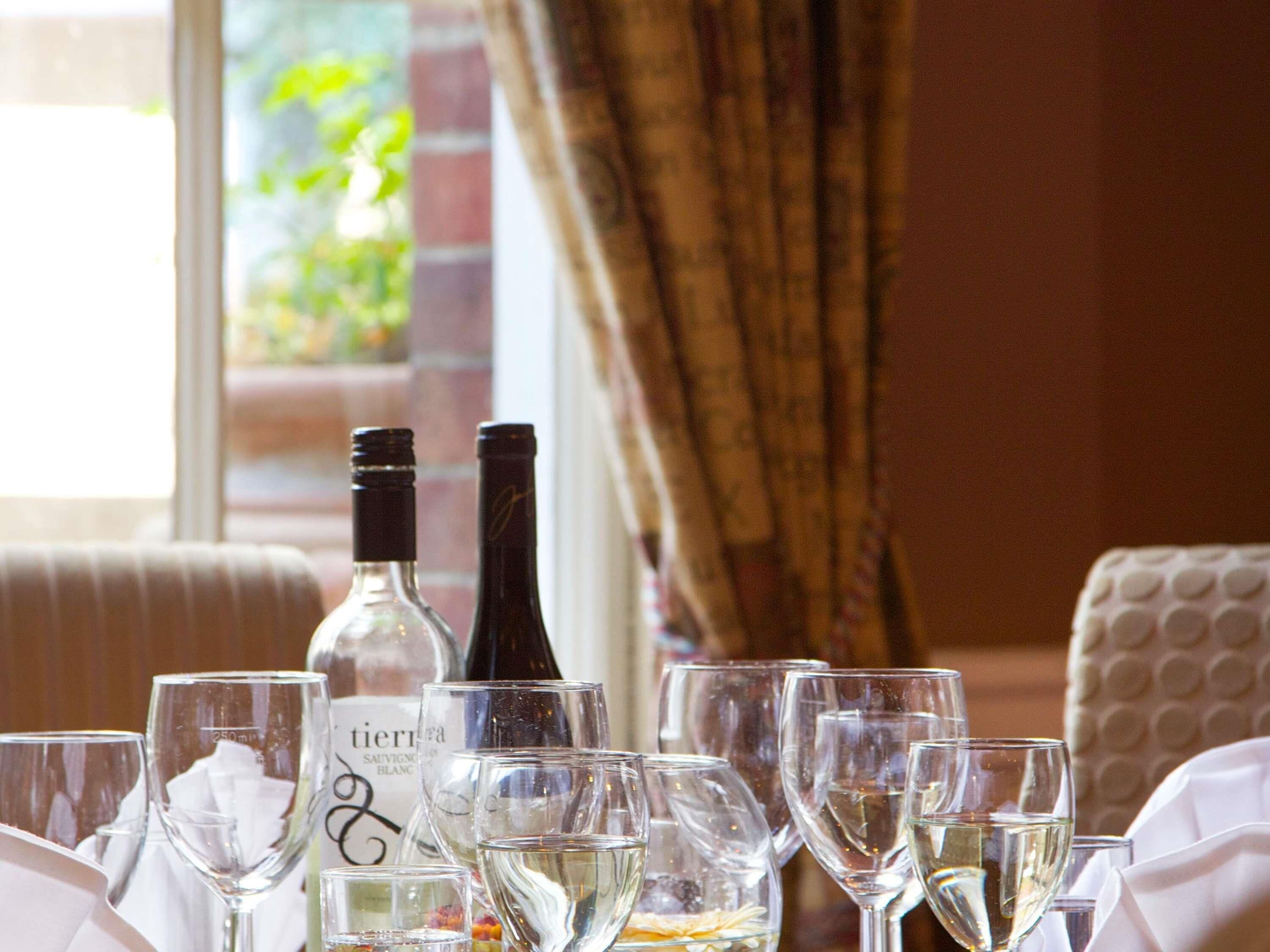A table set with wine glasses and bottles, a window with a view of greenery, and a patterned wall.