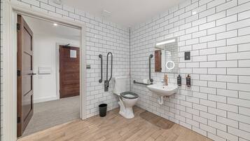Un baño moderno con azulejos blancos tipo metro, suelo de madera, inodoro, lavabo y espejo.