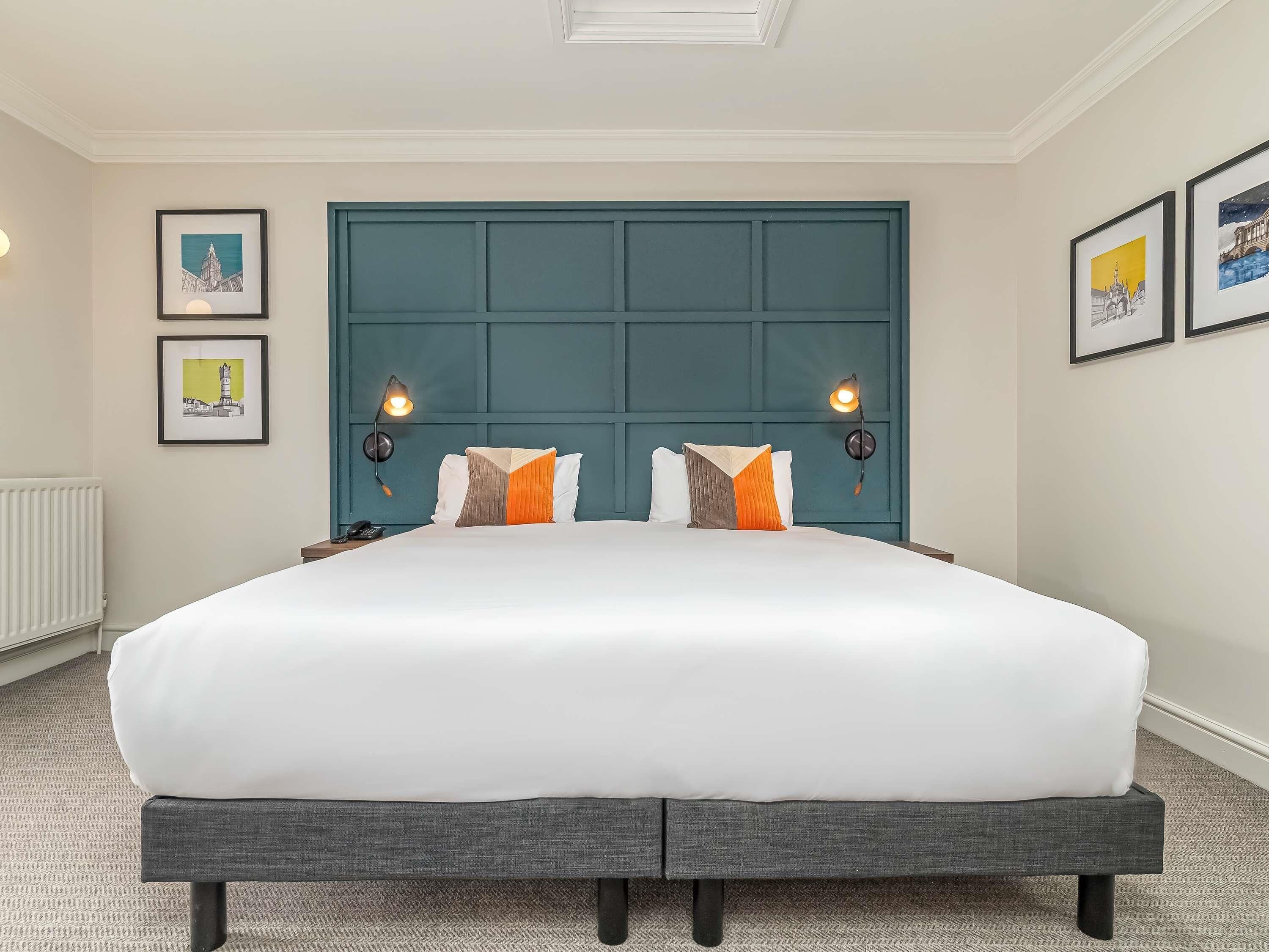 A hotel room with a large bed, two bedside lamps, a headboard, and framed pictures on the walls.