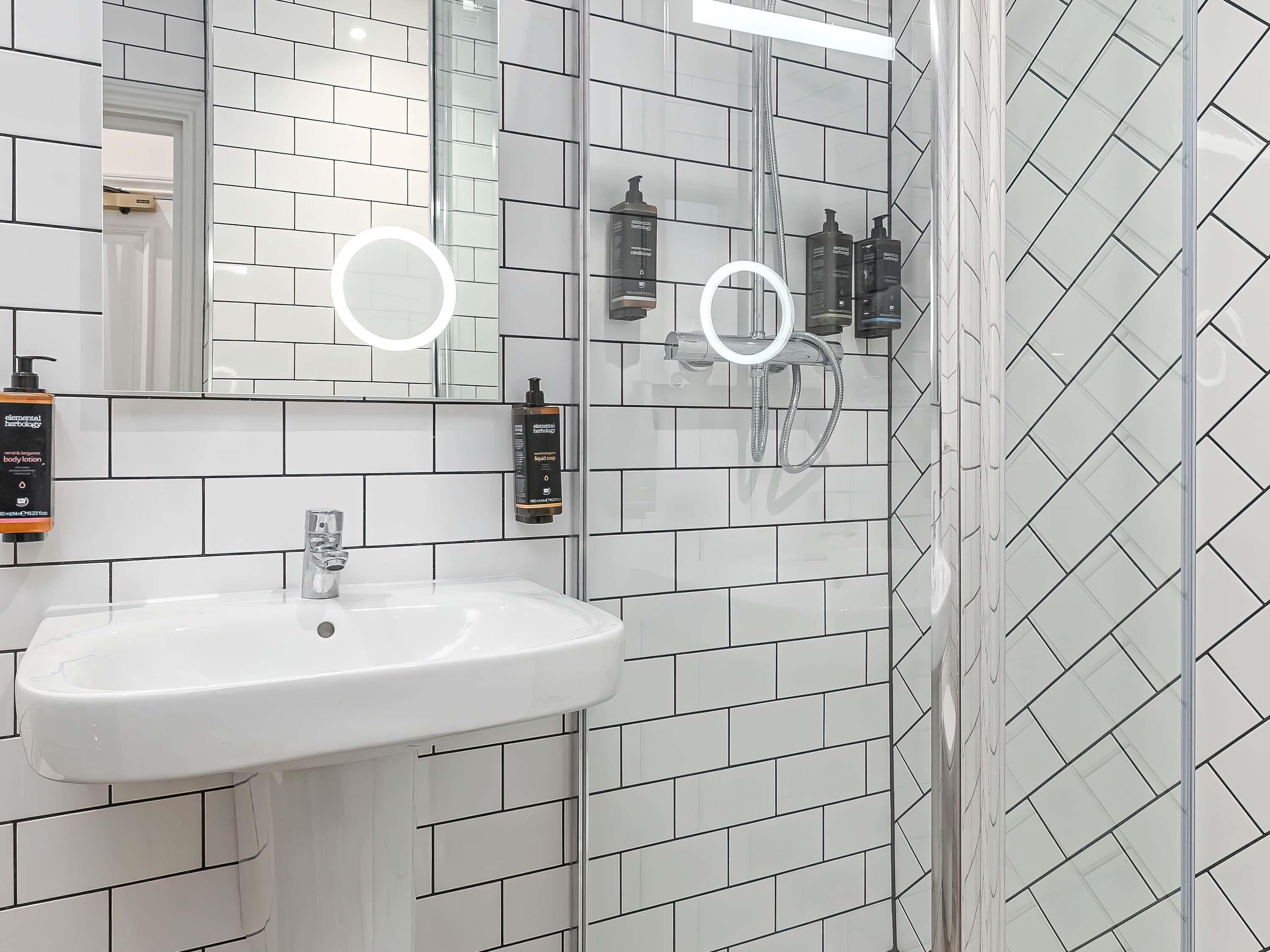A bathroom with a white sink, two mirrors, and a shower area.