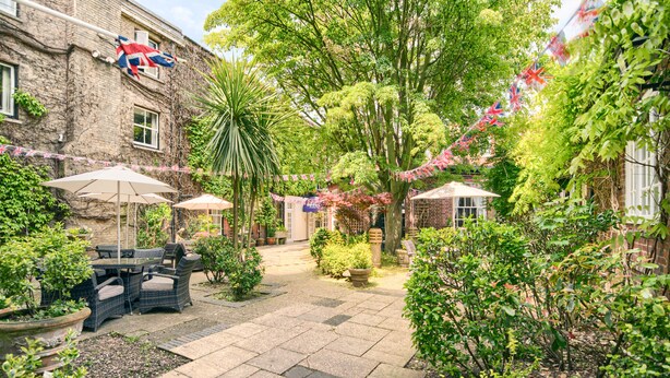 A courtyard with outdoor seating, potted plants, and a brick building with flags. - Mercure White Hart Hotel Salisbury and Apartments (Salisbury)
