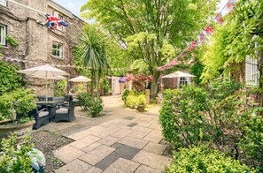 A courtyard with outdoor seating, potted plants, and a brick building with flags.