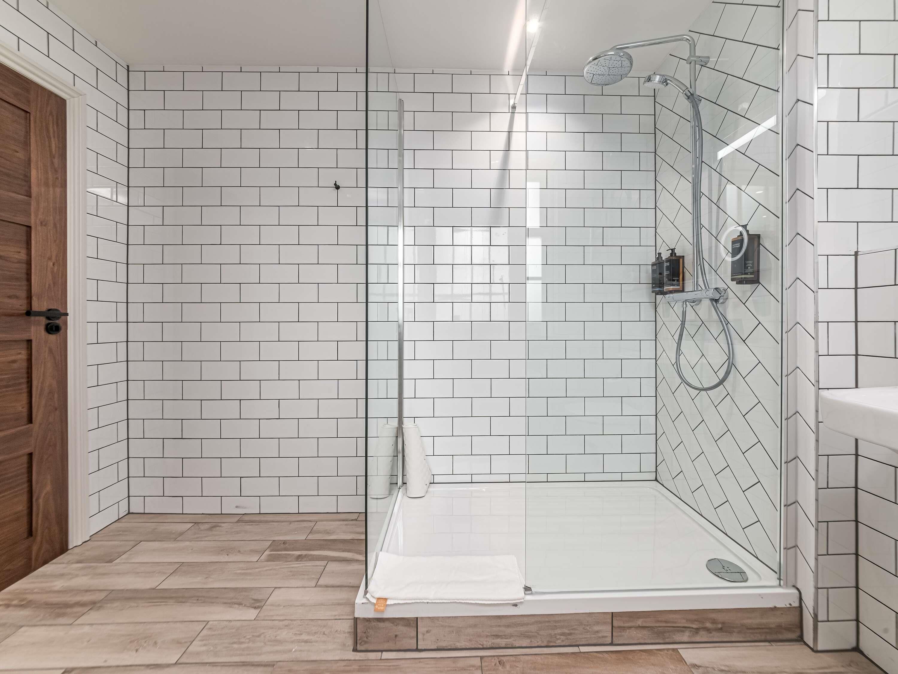 Un baño moderno con paredes de azulejos blancos, una cabina de ducha de vidrio y una puerta de madera.