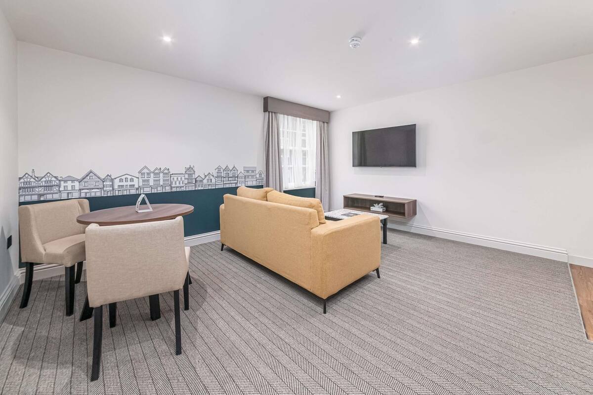 A modern living room with a sofa, chairs, a coffee table, a flat-screen TV, and a cityscape wall art.